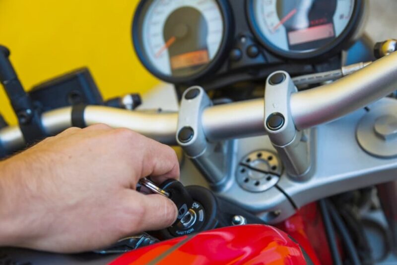 A person's hand turning the ignition key on a motorcycle's handlebar