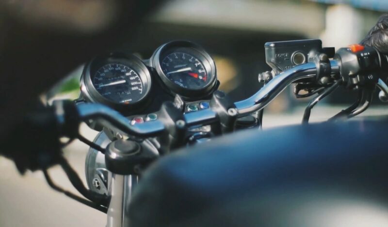 A close-up of motorcycle handlebars showing gauges and switches